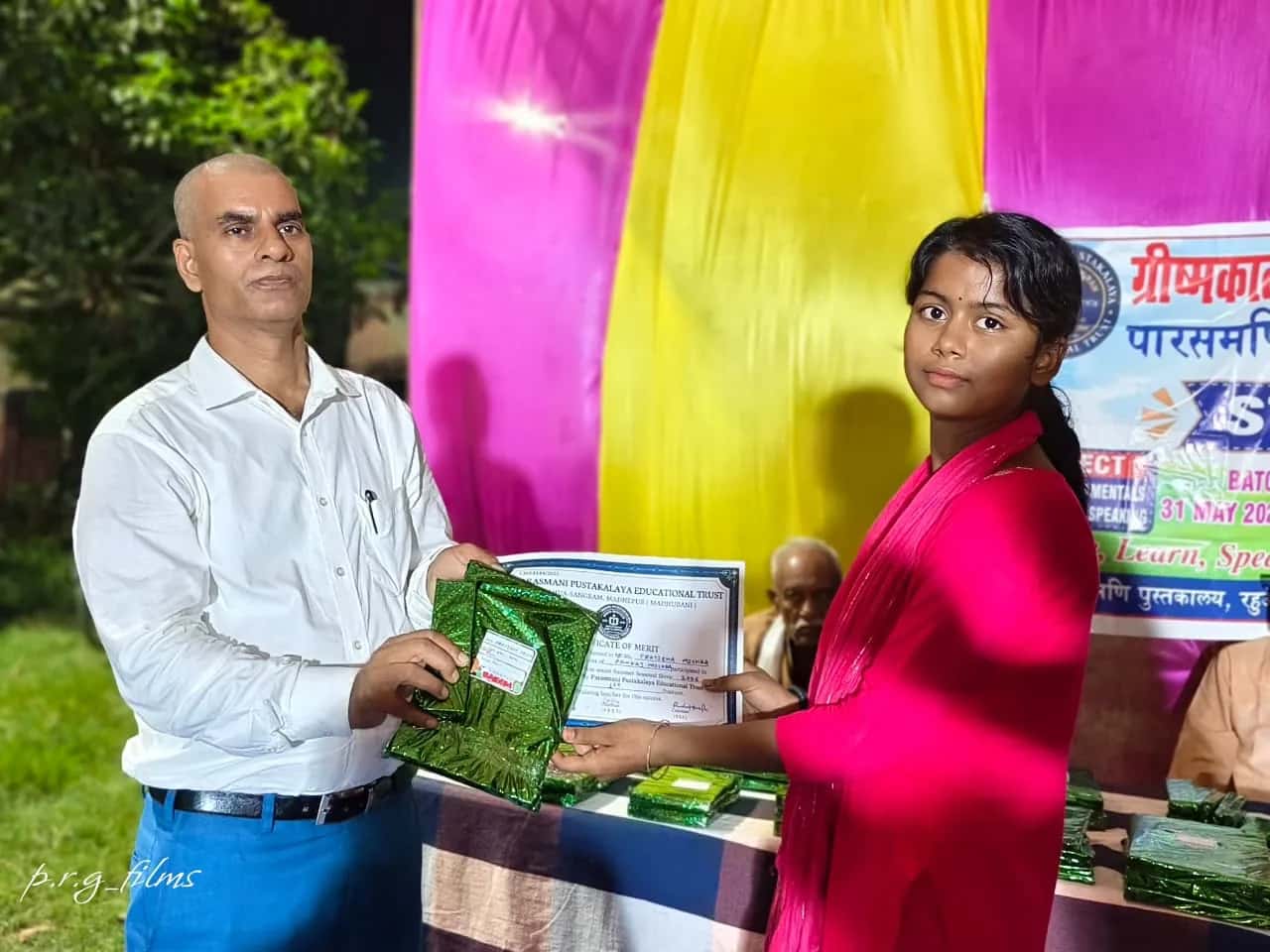 A student holding her certificate and prize with a presenter at Summer Shivir