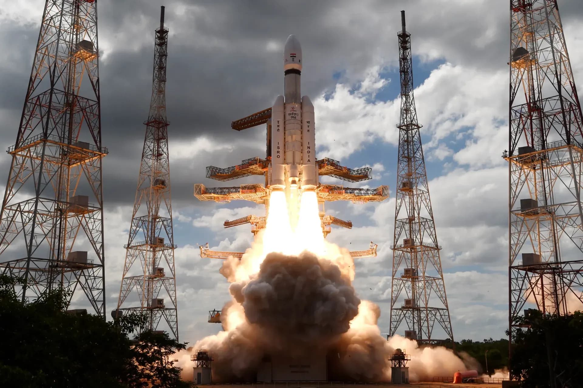 An ISRO rocket with Chandrayan 3 lifts off amid bright flames and billowing smoke.